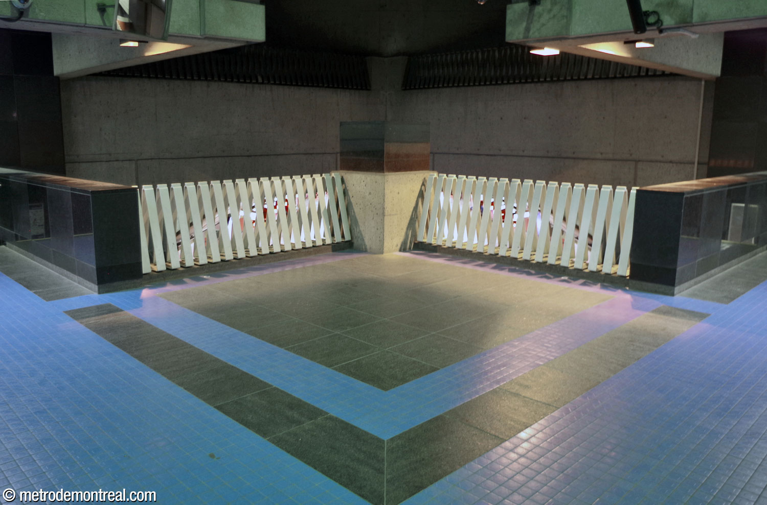 The overlook onto the platforms is located at the northern point of the 45-degree square of the ticket hall volume, which juts out over the tracks. The parapet consists of white enamelled steel grilles, and the concrete tip is surmounted by a black granite cube.