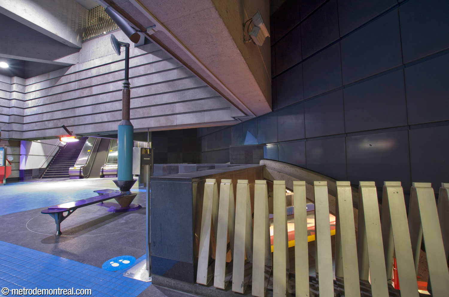 A symmetrical but less prominent overlook is located at the rear of the ticket hall, in the fare-free zone. Here, the southern tip of the mezzanine contacts the spandrel wall over the trainroom vault, which is clad in dark blue enamelled steel panels like those that make up the stripe along the platform walls. Météore Design's sculptural clock Lieu de rendez-vous is located here.