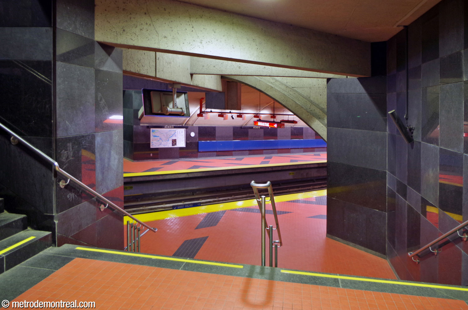 The stairwells down to the platforms—here, the Saint-Michel platform—are enclosed in full-height walls clad in the platforms' black checkerboard granite.