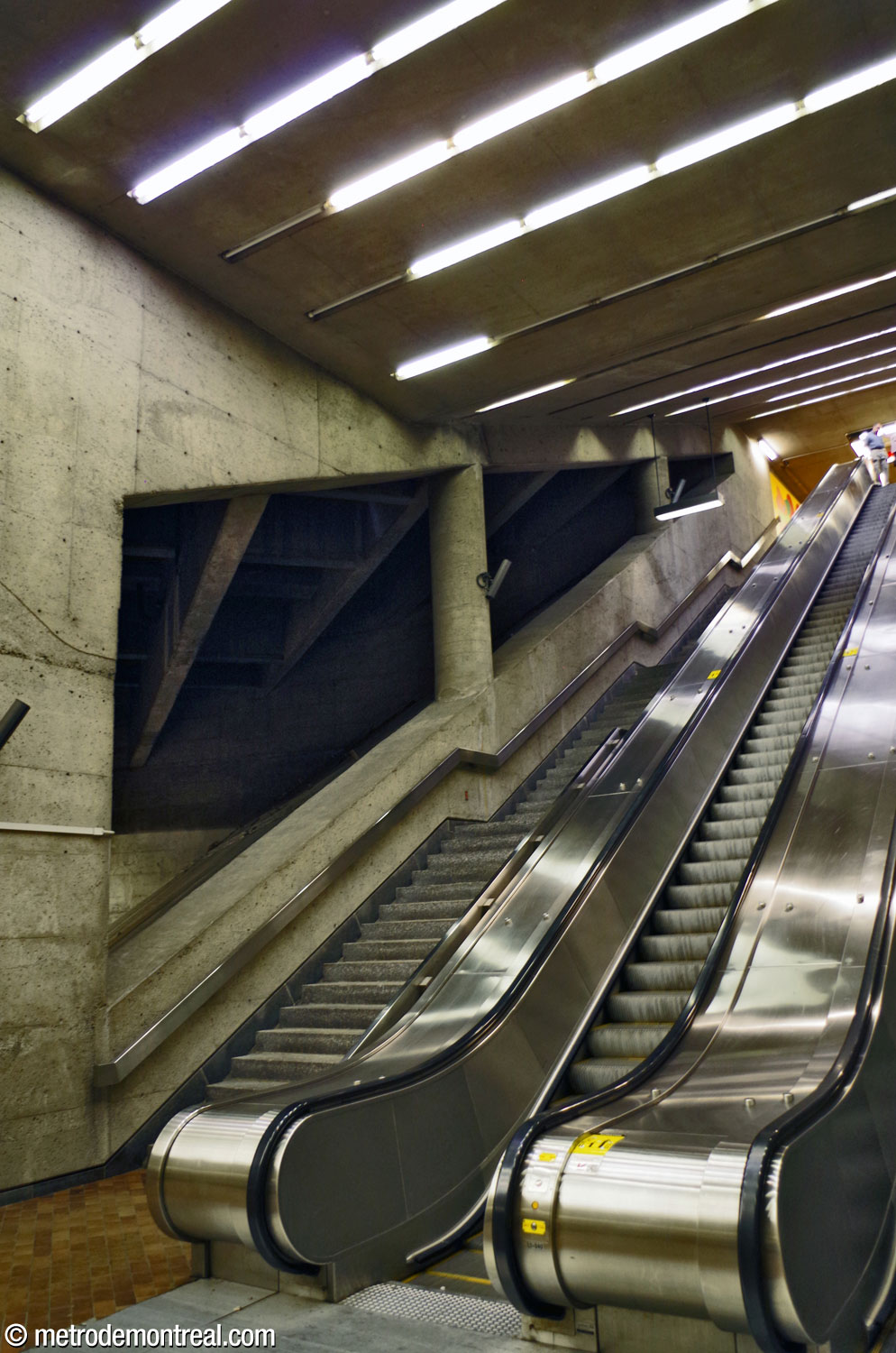 Le pied des escaliers mécaniques menant à la mezzanine, avec vue en contre-plongée vers l'espace triangulaire.