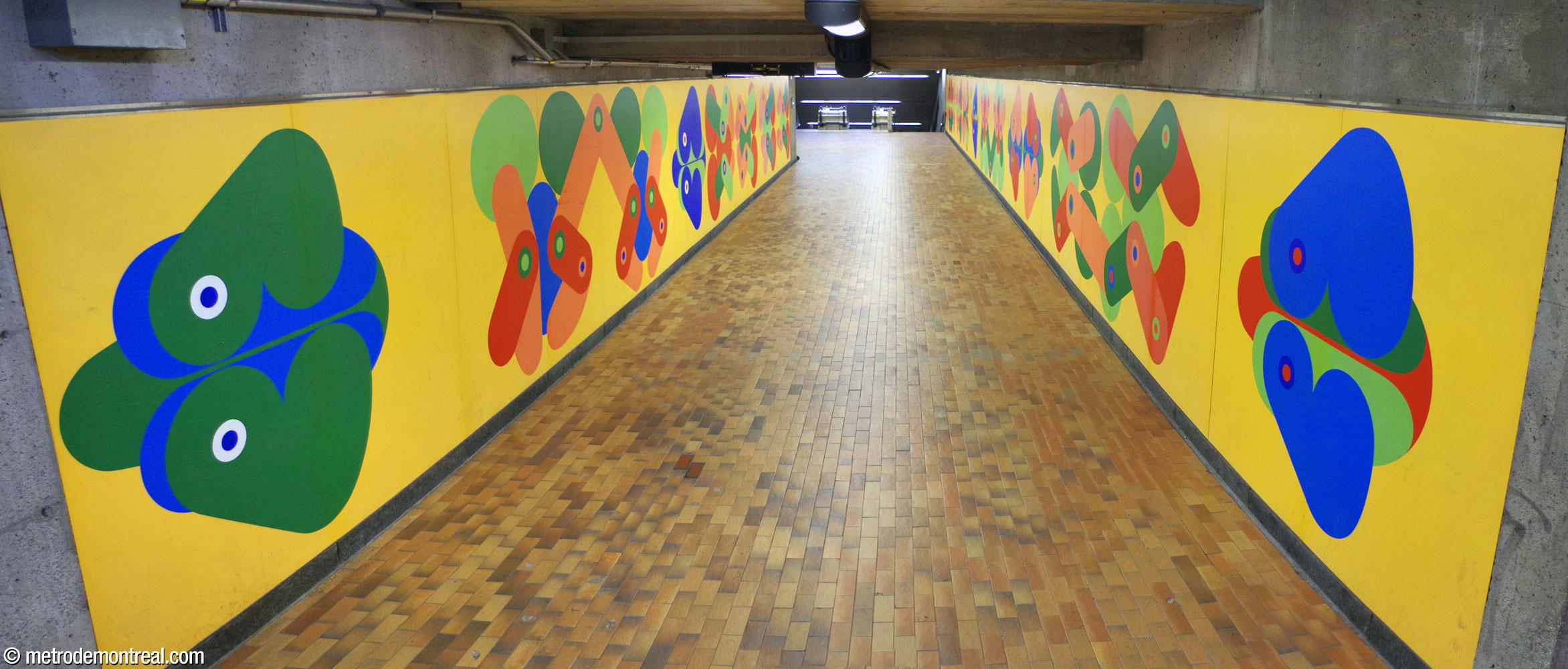Le corridor reliant l'escalier fixe vers l'édicule aux escaliers mécaniques vers la mezzanine. Chaque côté arbore l'un des deux éléments principaux de l'ensemble mural Un parcours sur l'olympisme, œuvre de Guy Montpetit.