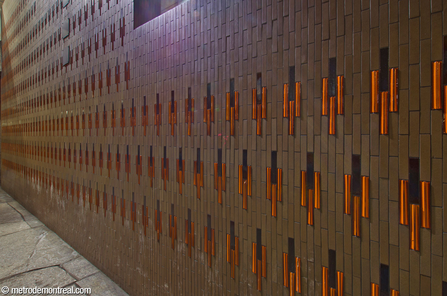 Le carrelage céramique des murs-écran longeant les escaliers latéraux entre la passerelle et les quais. Créé par Claude Vermette, le motif présente des motifs de flèche constitués de carreaux orange et brun foncé, sur un fond gris-brun.