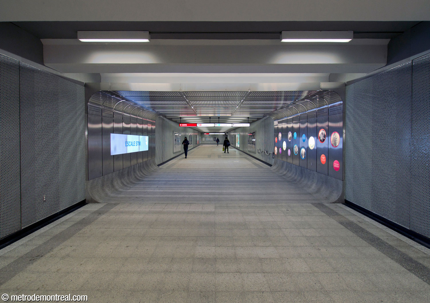 La vitrine historique Escale STM, située dans le couloir vers la sortie Saint-Denis. Un tunnel en acier inoxydable présente un afficheur multimédia d'un côté, et de l'autre, un jeu de hublots-présentoirs pouvant accueillir des objets ou des affiches.
