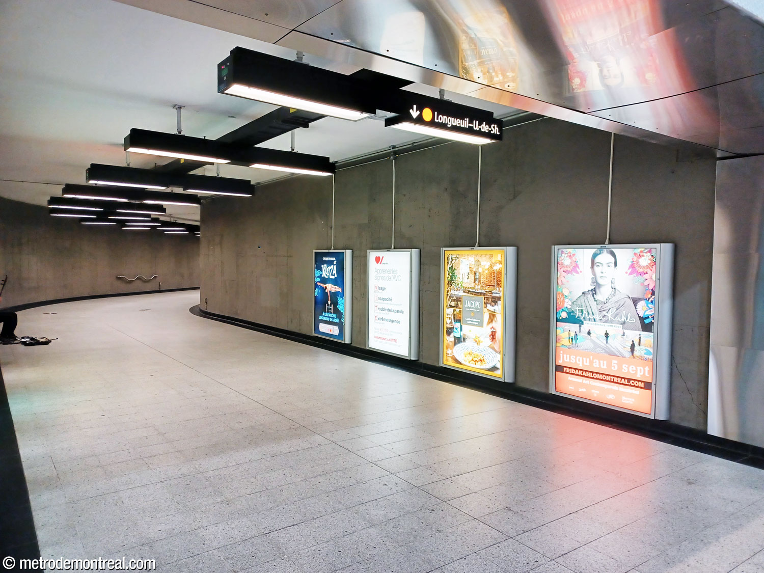 Une partie du long corridor courbe entre le pied de la volée principale d'escaliers mécaniques vers la ligne jaune et le couloir collecteur menant vers les quais de la ligne jaune.