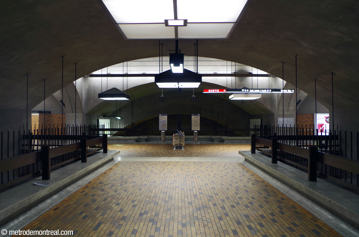 Vue vers l'ouest depuis le centre du niveau mezzanine le long du passage central, soulignant l'aménagement symétrique des voûtes de la station. La voûte transversale ouest accueille les accès vers l'édifice Place du Canada et le Château Champlain (gauche) et vers le long corridor et escalier vers la sortie Peel, l'édifice Gare Windsor, le Centre Bell et le 1250 René-Lévesque. Les passages du niveau mezzanine sont bordés de bancs sur toute leur longueur et donnent sur le niveau des quais en contrebas.