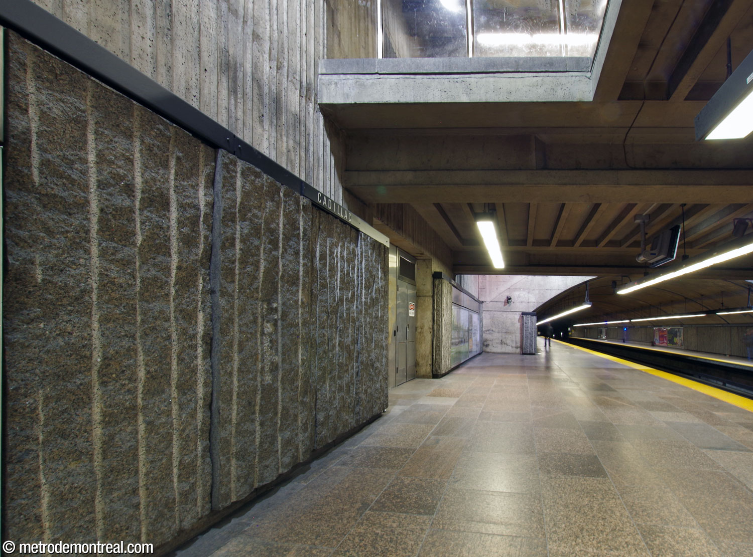 Underneath the mezzanine in the central volume, the rough granite dados on the platform walls are taller, and as a result the nameplates are higher, than in the mined sections of the trainroom.