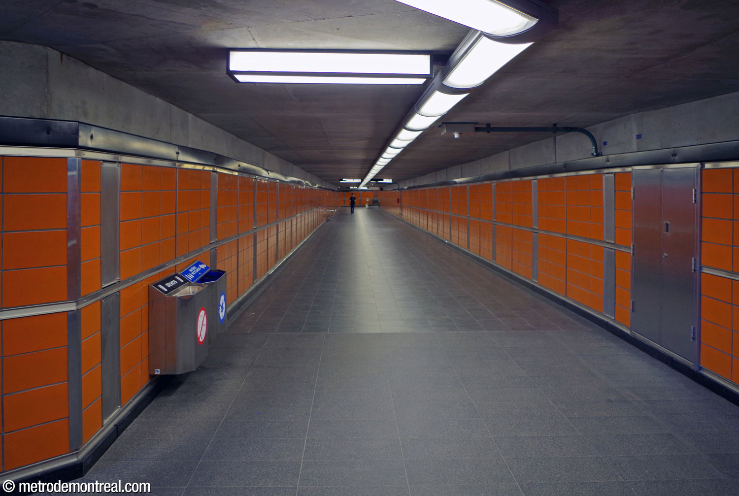 Un tronçon du tunnel vers l'édicule secondaire. Comme aux quais, les murs sont revêtus de terre cuite glacée orange avec des joints en acier inoxydable, et les planchers sont en granit noir.