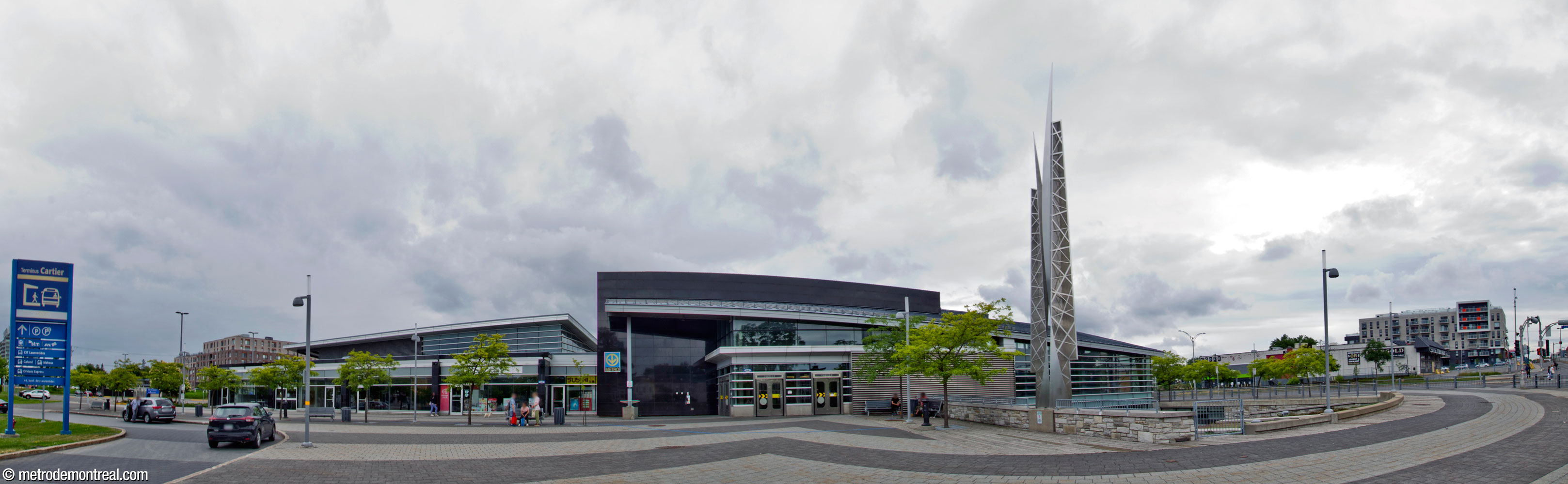 Vue d'ensemble de la façade est de l'édicule principale, face au boulevard des Laurentides. Au centre, l'entrée sud de l'atrium de la station de métro; à droite, la sculpture L'Homme est un roseau pensant III de Jacek Jarnuszkiewicz surplombe le jardin surbaissé. À gauche, l'aile de l'édicule qui accueille le terminus d'autobus se projette vers le sud, devant un débarcadère.
