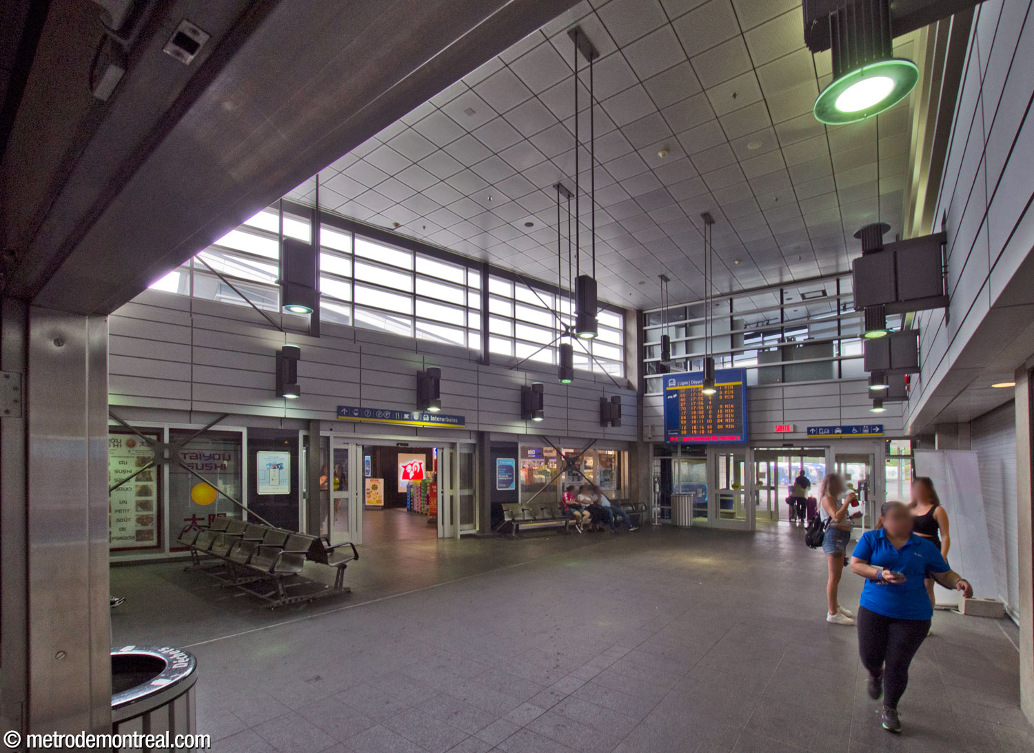 Les portes à partir de l'atrium du métro ouvrent sur cette aire centrale d'attente intérieure pour le terminus d'autobus. Revêtue en tons de gris et éclairée par une claire-voie, elle dessert surtout les passagers des autobus de la STL. Un local de répartiteurs d'autobus est visible à l'étage au-dessus de la sortie vers les jetées du terminus (centre-droite). Au centre gauche, les portes vers l'aile sud du terminus.