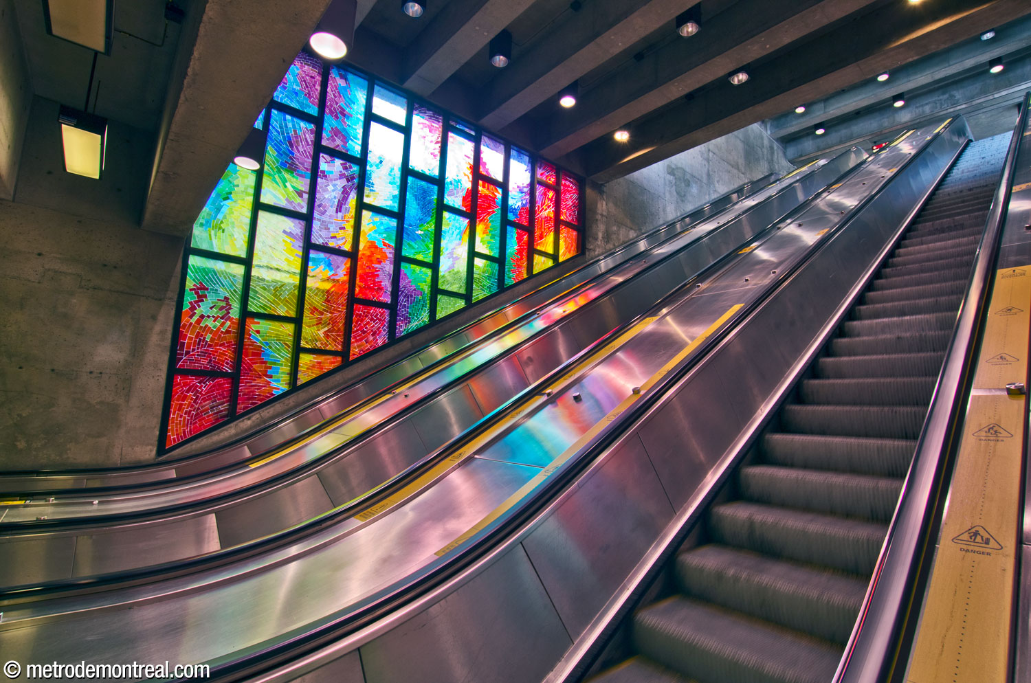 The escalator well between the ticket hall and the headhouse. Near its foot is Octavie, a stained glass window by Mario Merola and Pierre Osterrath.