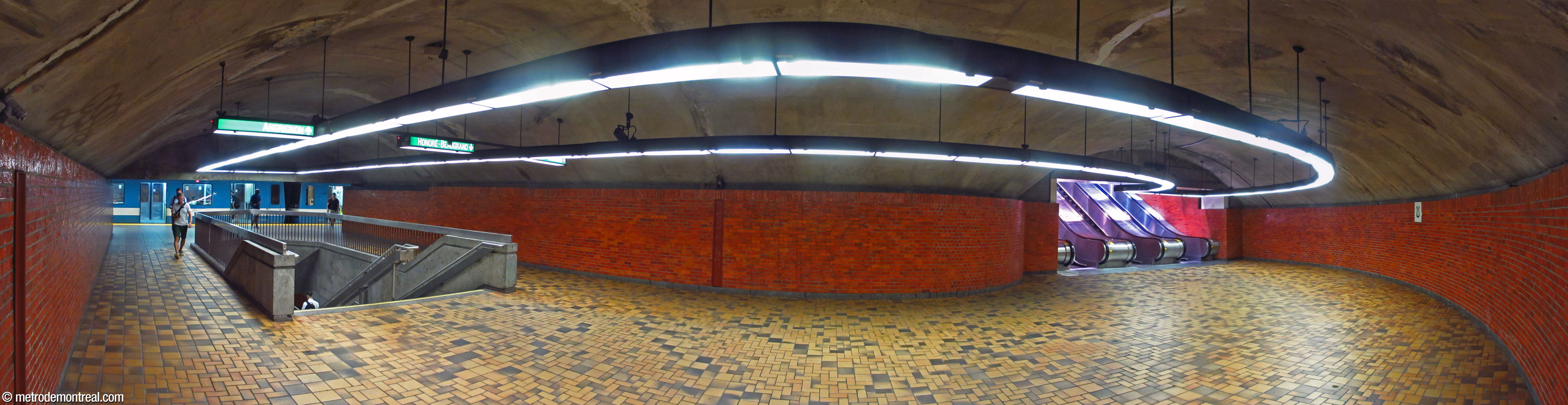 Panorama of the curved hallway between the foot of the escalators and the upper platform. The staircase to the lower platform occupies the centre of the hallway.