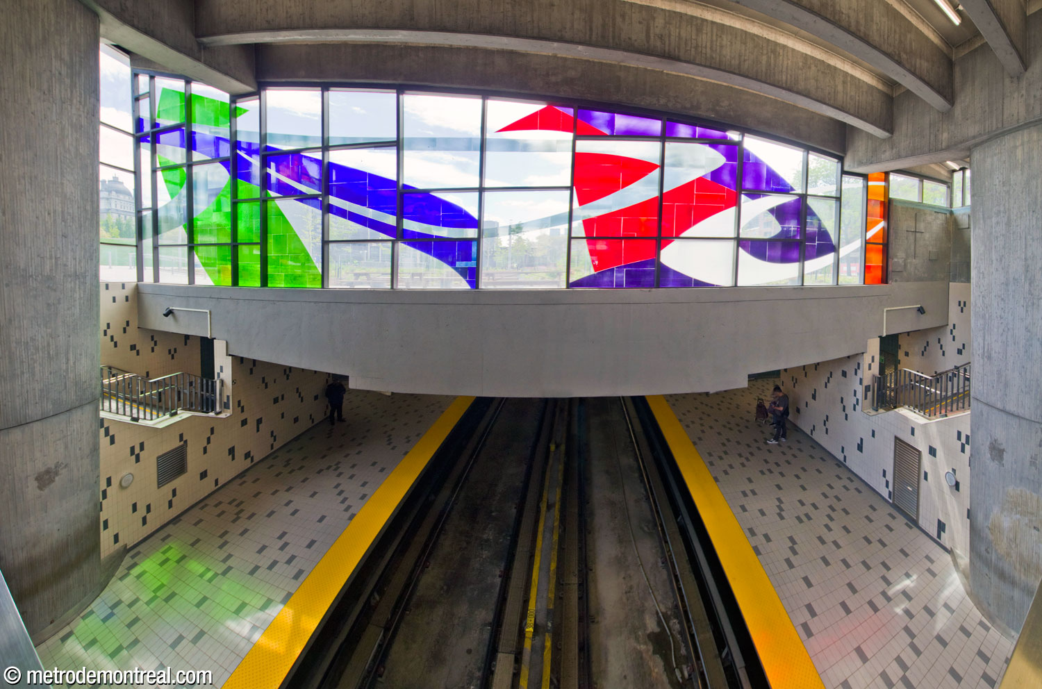 Part of the stained-glass window by Marcelle Ferron, on the west wall of the headhouse, above the overlook from the ticket hall onto the platforms. Also visible above the tracks is the profile of the unusual ceiling of the trainroom, angled up to the sides from a lowered central section.