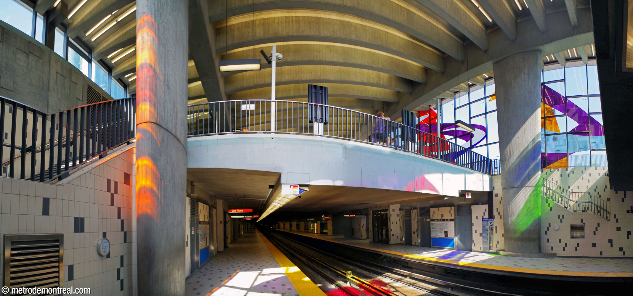 View upward from the platforms toward the headhouse, showing the play of coloured light from Marcelle Ferron's stained-glass window across the platforms and tracks. The shallow platforms continue eastward under the ground floor. Note the oval columns, tapered downward, that support the western corners of the roof and continue down to the platforms.