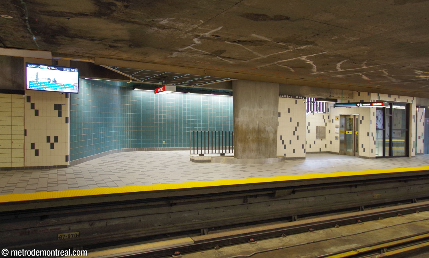The foot of the elevator and eastern stairwell on the Montmorency platform, seen from across the tracks. Note the tapered foot of one of the columns supporting the roof, descending through the floor of the ticket hall.