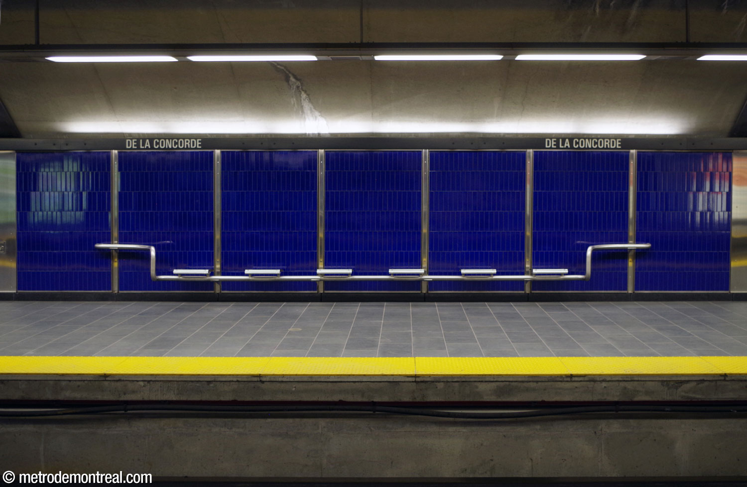 One of the station's stainless-steel benches, similar to those in the other Laval stations, against the deep blue walls of the platform.