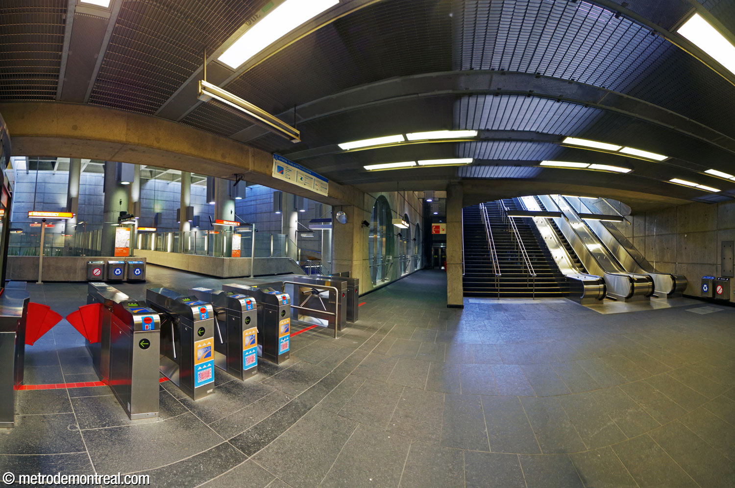 The station's ticket hall is located at the foot of the stairs and escalators from the surface (right). The turnstiles lead directly to the crossover (left). At centre, a hallway leads to the elevator to the surface.