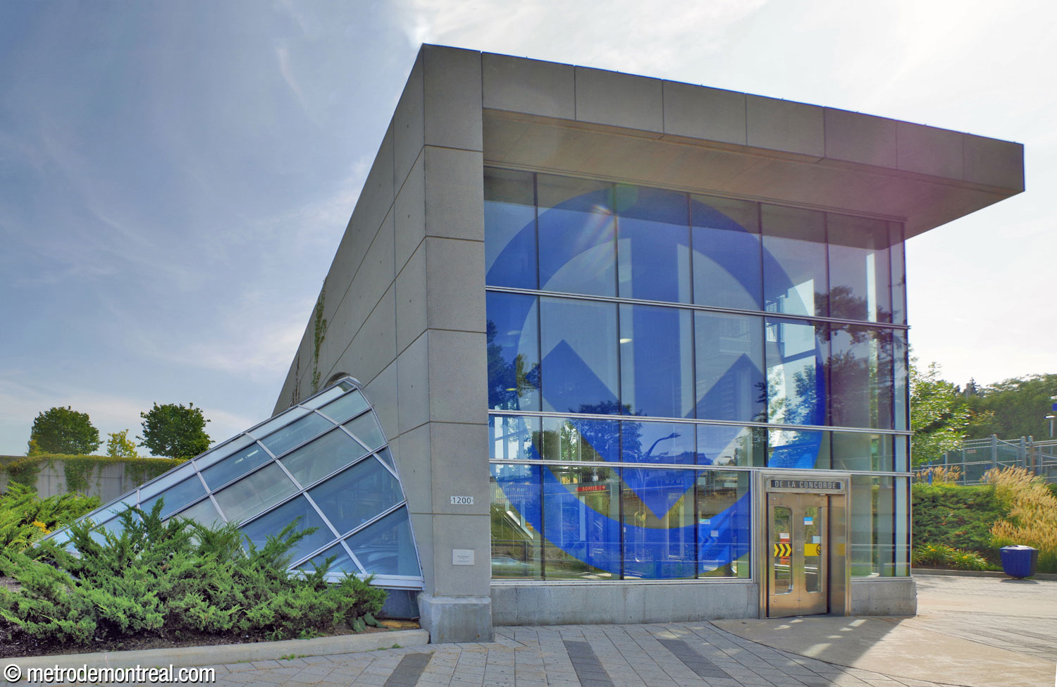 Front view of the headhouse and its huge metro logo. The glass canopy of the stairwell to the ticket hall is at left.