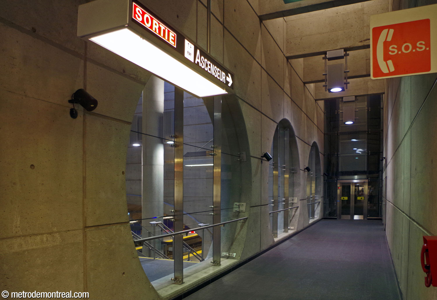 The hallway from the ticket hall to the elevator to the surface. At left, three large circular windows overlook the main volume.