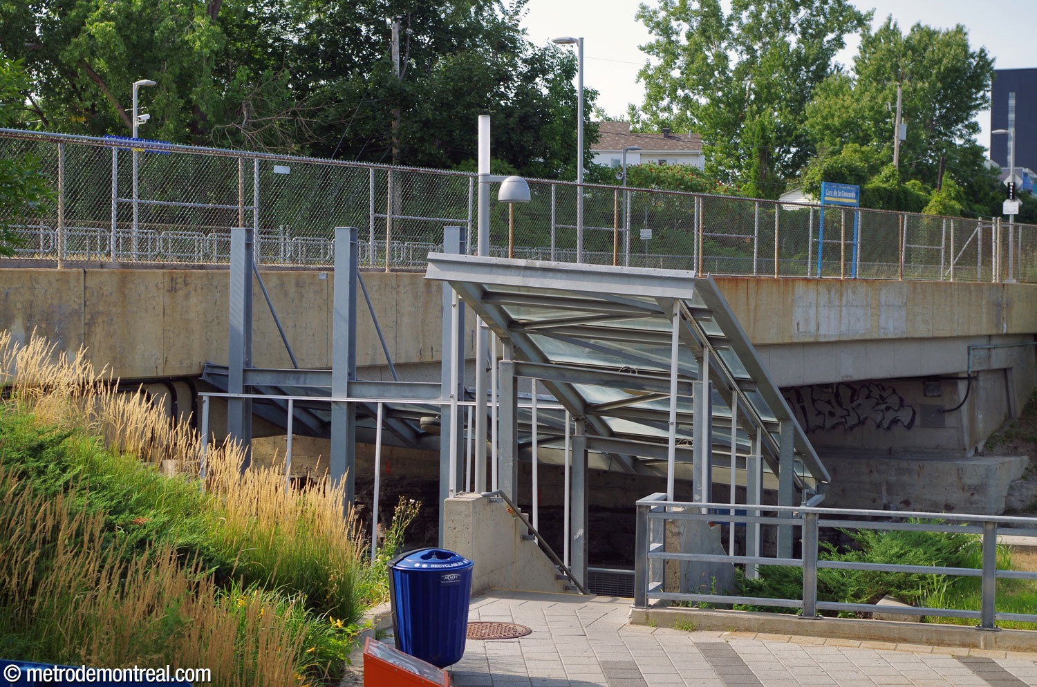 A covered staircase heads down from an open area next to the lower level of the headhouse, leading to a walkway to the inbound platform and the Boulevard de la Concorde sidewalk.