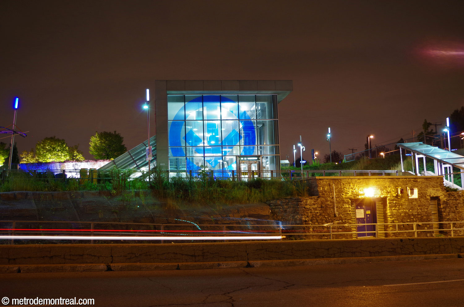 The glass wall on the front of the headhouse shines out at night, highlighting the metro logo emblazoned on it.