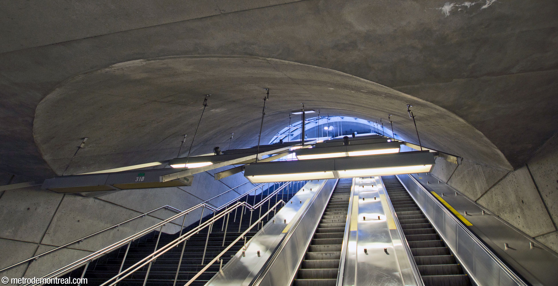 The slanted cylindrical shaft enclosing the stairs and escalators up to the headhouse intersects with the flat ceiling of the ticket hall.