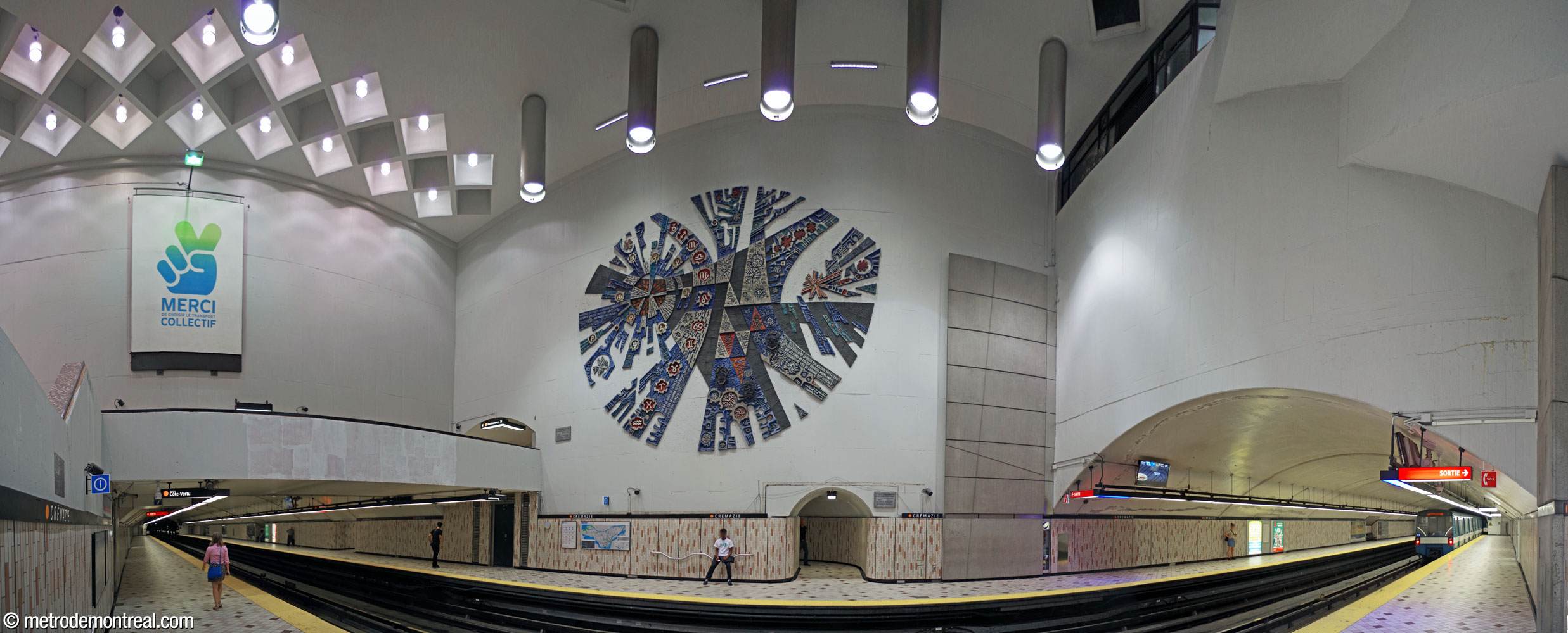 Le grand volume de la station vu depuis le quai Côte-Vertu. Les portions de la nef construites en tunnel s'étendent à gauche, sous la passerelle, et à droite. Au centre, la murale Le poète dans l'univers occupe le mur au-dessus du quai Montmorency. Le décor consiste de béton peint de blanc en haut, avec du carrelage céramique de couleur crème, beige et pêche sur les lambris et au sol.