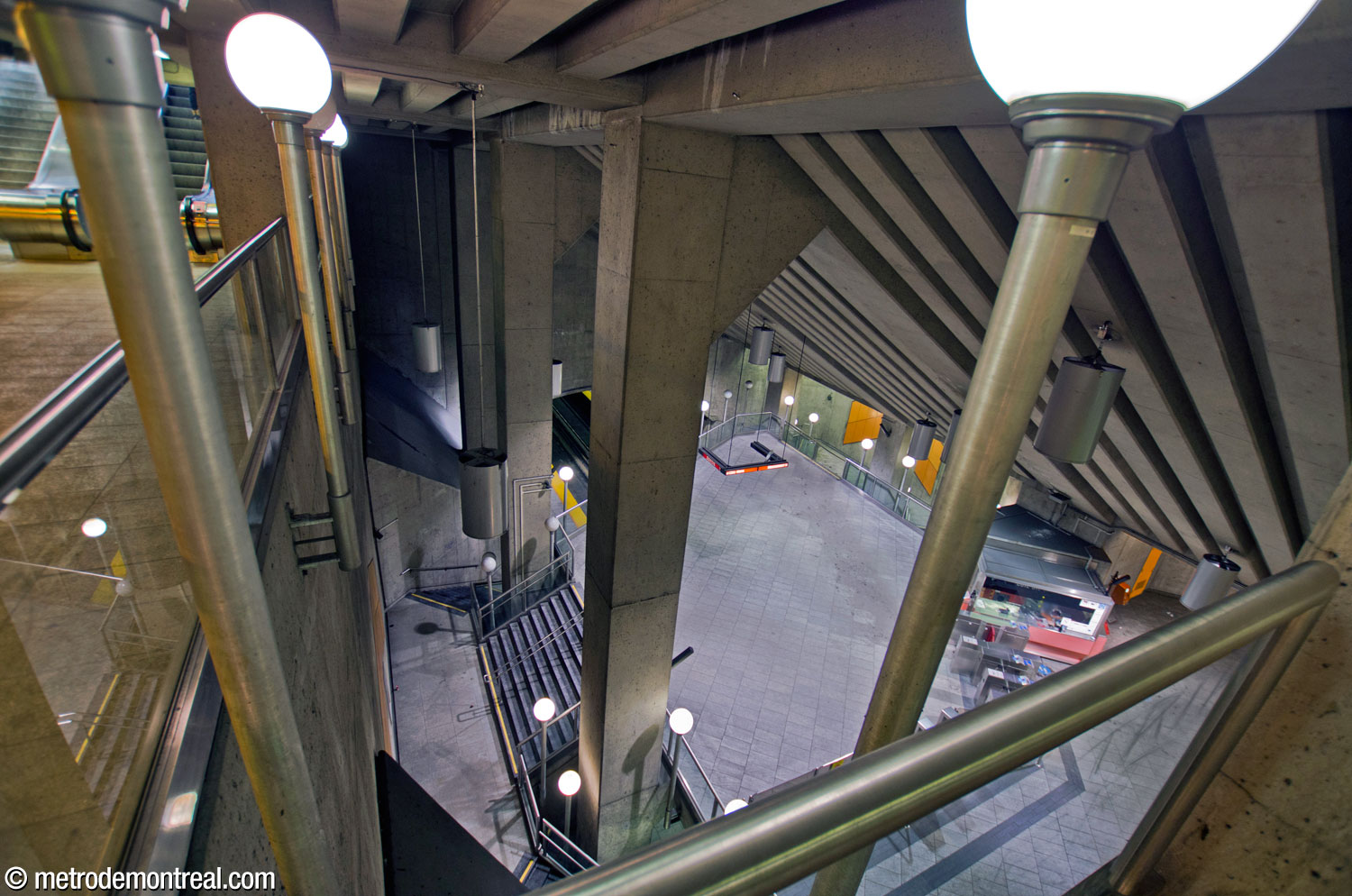 Vue en plongée depuis le passage au-dessus du grand volume. On y voit les colonnes qui portent le toit de la station, dont les pieds sont entourés par les escaliers vers le quai Côte-Vertu.