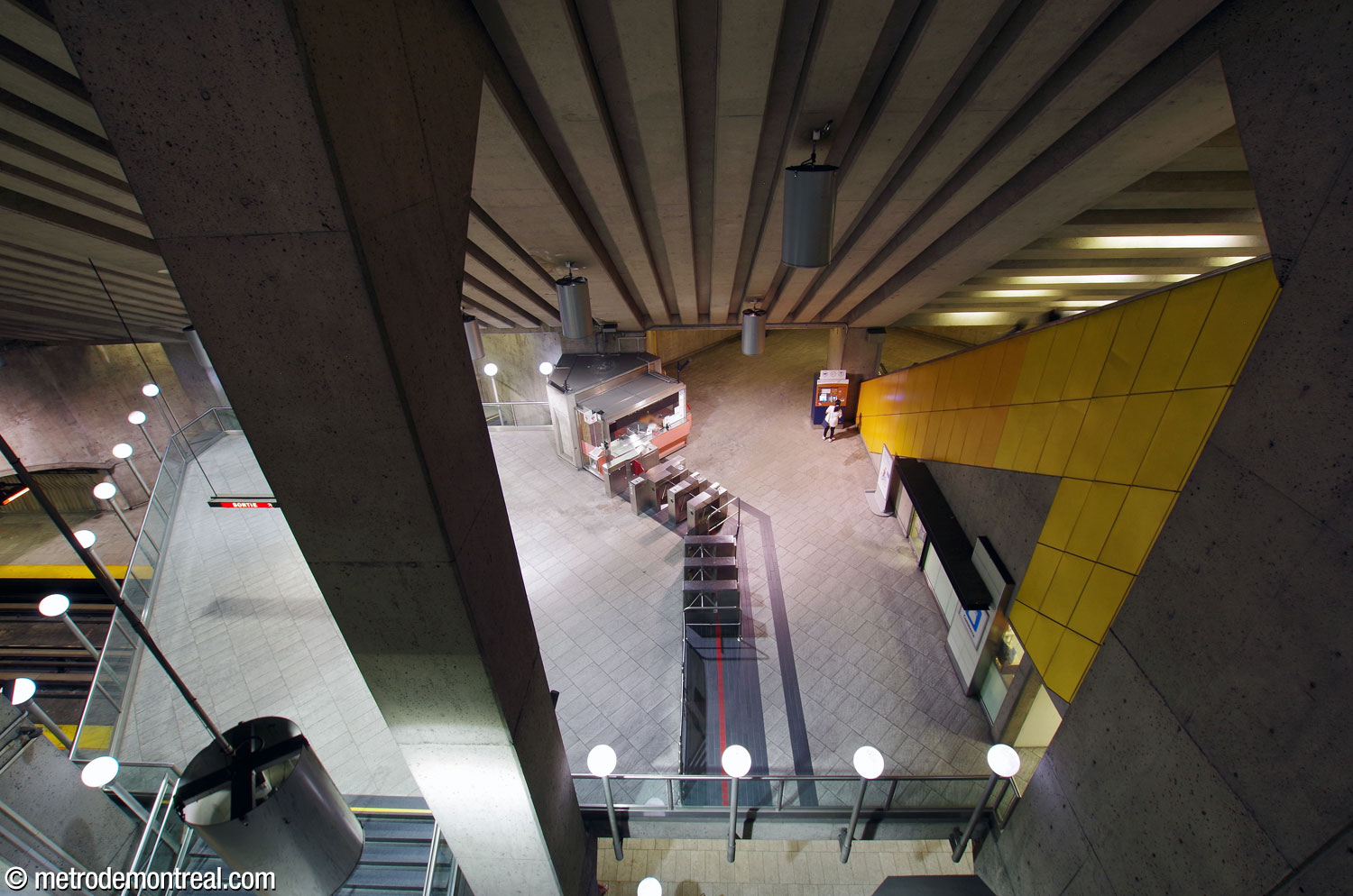 Vue en plongée sur la mezzanine depuis le passage au-dessus du grand volume; on voit en contrebas la barrière de perception de la billetterie.
