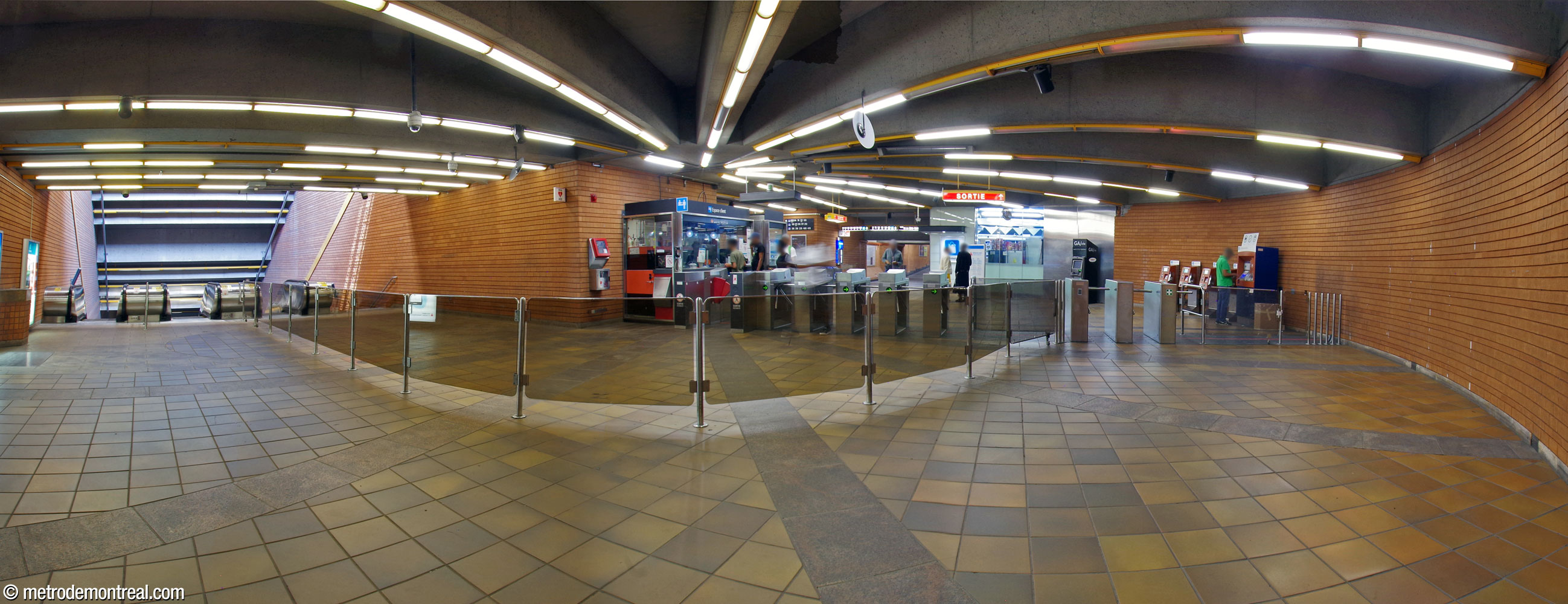 Panorama à partir de l’arrière de la billetterie. On en voit le plan semi-circulaire qui décrit un parcours courbe direct entre les tourniquets (droite) et les escaliers vers les quais (gauche). On note les barrières qui séparent la circulation entre les passagers qui entrent et ceux qui sortent.