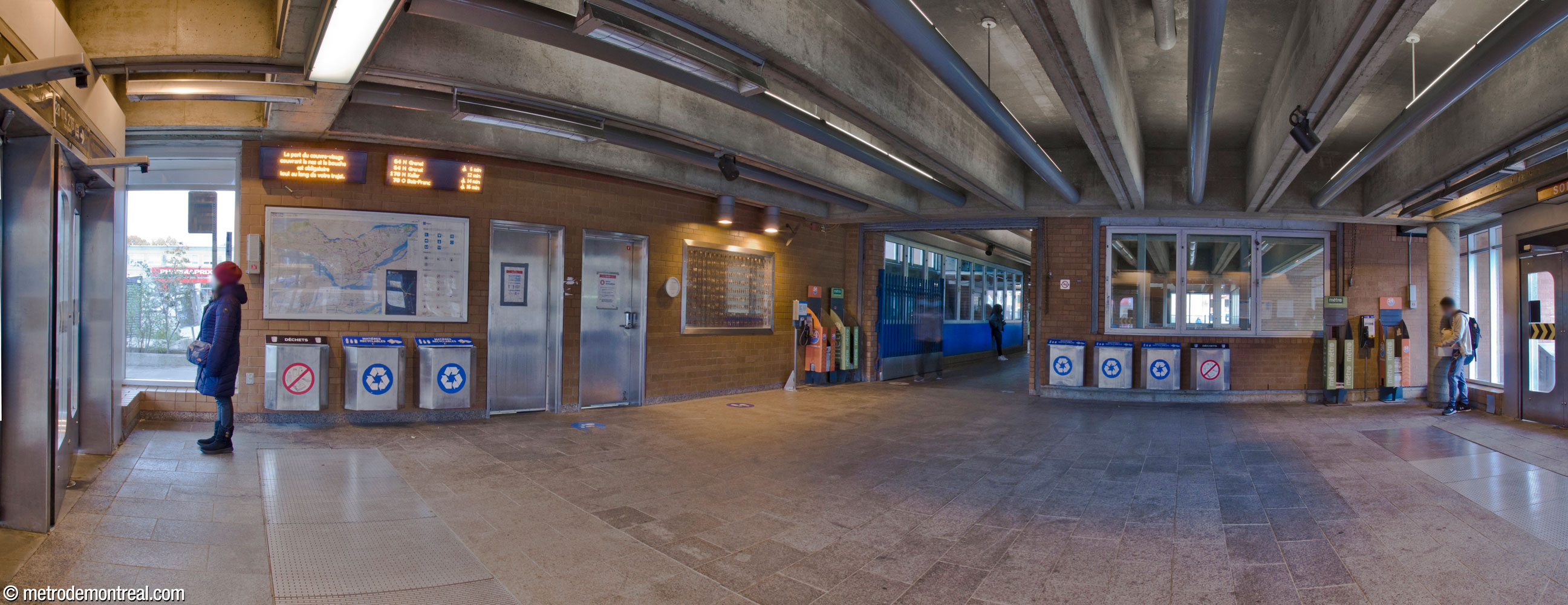 Intérieur de l'aire d'attente du terminus d'autobus, dans la partie nord de l'édicule Côte-Vertu Nord. L'espace vitré à droite est le volume principal, qui se projette vers sa claire-voie; le couloir au centre droite est en fait une passerelle qui traverse le volume. Au mur (centre), à gauche de la passerelle, on trouve l'œuvre L'Homo urbanus d'Éric Lamontagne.