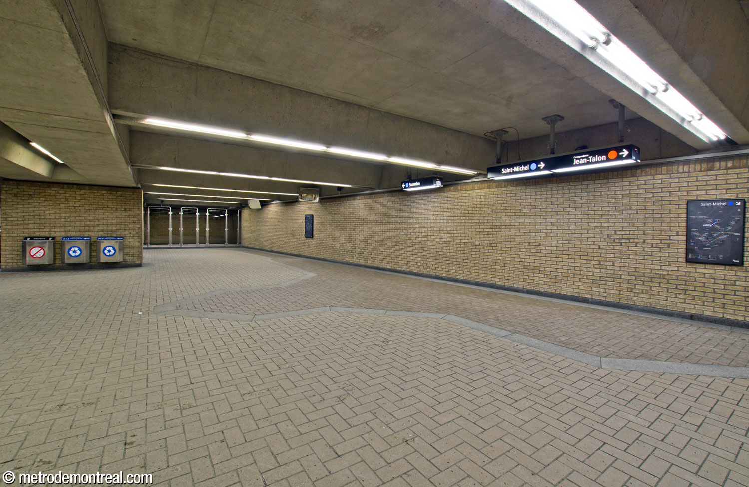 The wide, flat wall at the rear of the ticket hall. The pavement stones in the floor tile pattern subtly lead toward the stairwells to the platform.