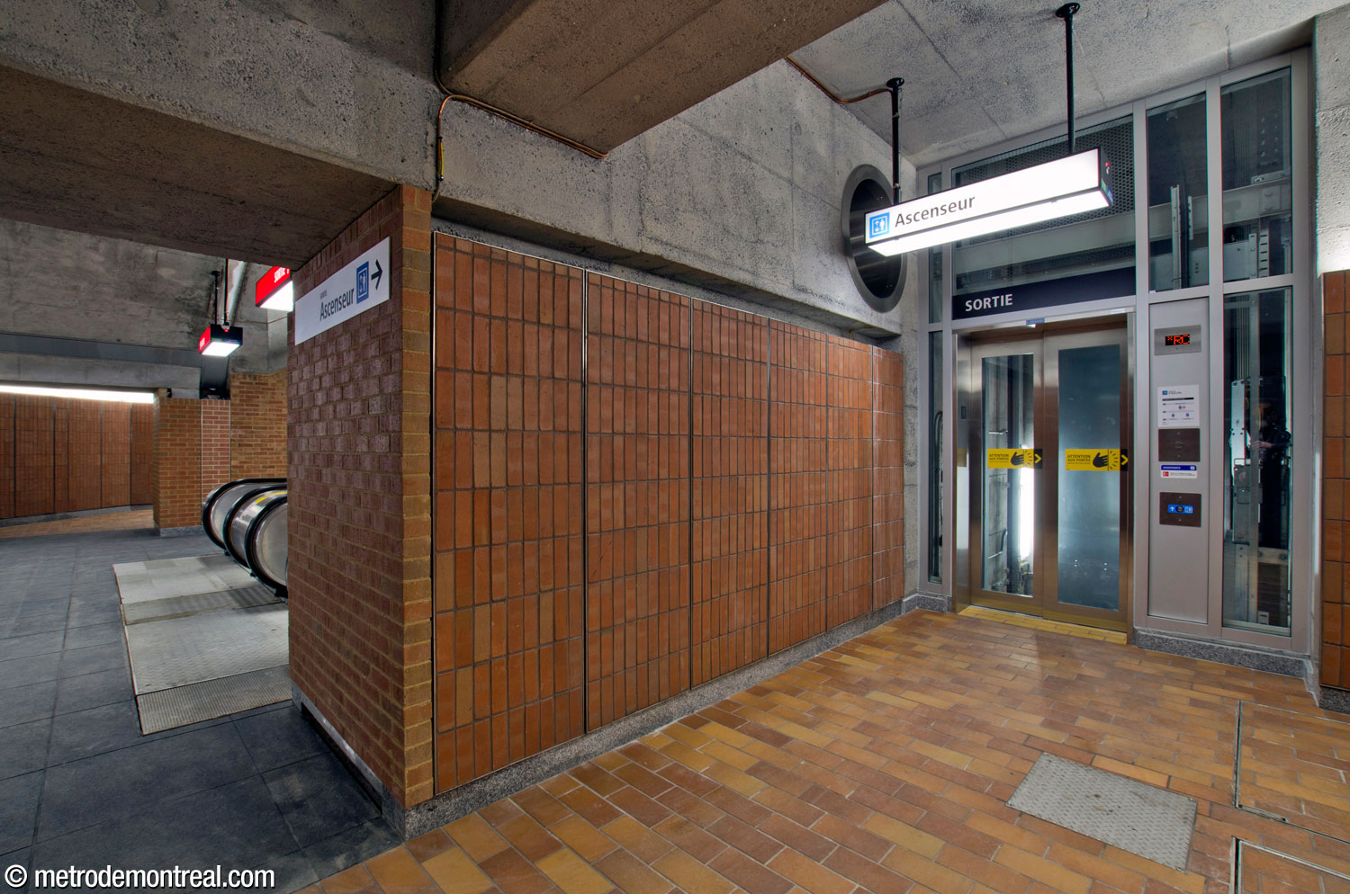An alcove to the right of the escalators leading up to the eastern access houses the elevator between the transept level and the surface. A porthole-like window to the escalator shaft is located above and to the left of the elevator.
