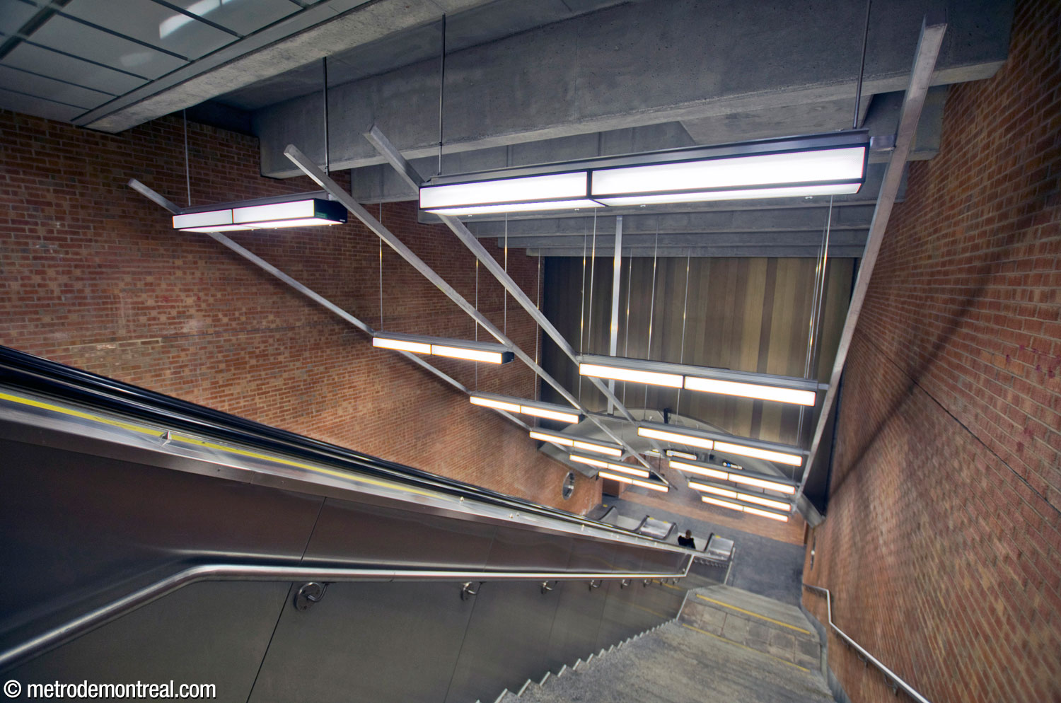The deep stair and escalator well between the eastern access and the trainroom. The rear wall of the volume is clad in the same brown metal as was used behind the sculpture Le Pélican in the other access. The light fixtures, with their overhead rails, were added at the same time as the elevators.