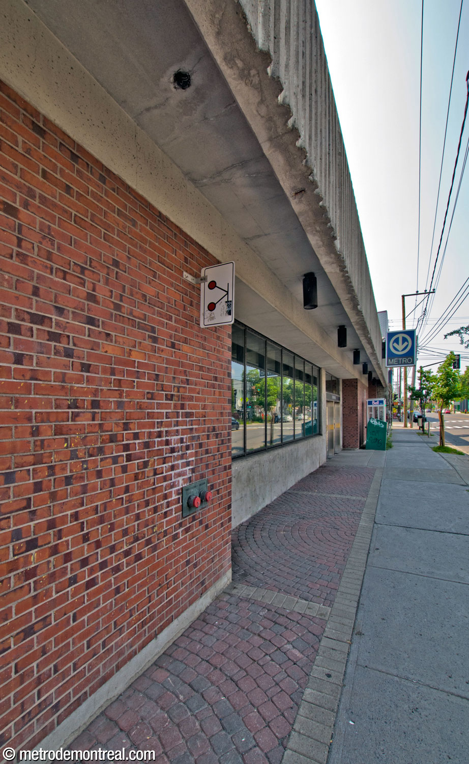The Rue Jean-Talon façade of the Louis-Hébert headhouse, with a shallow projecting roof. Notice the brickwork paving between the façade and the sidewalk.