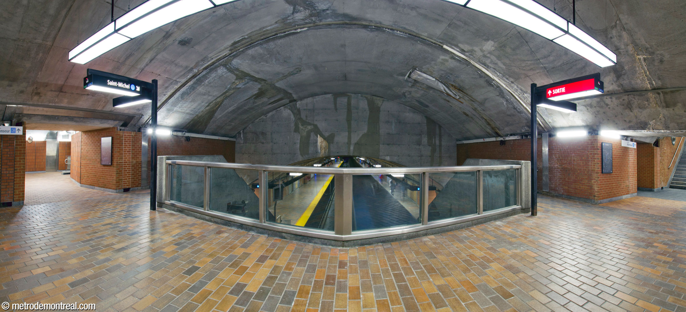 The balcony-style crossover in the eastern access is housed in a vault at the east end of the trainroom. At left and right, alcoves house elevators to the platforms. The glass and metal parapet over the tracks consists of two halves at oblique angles.