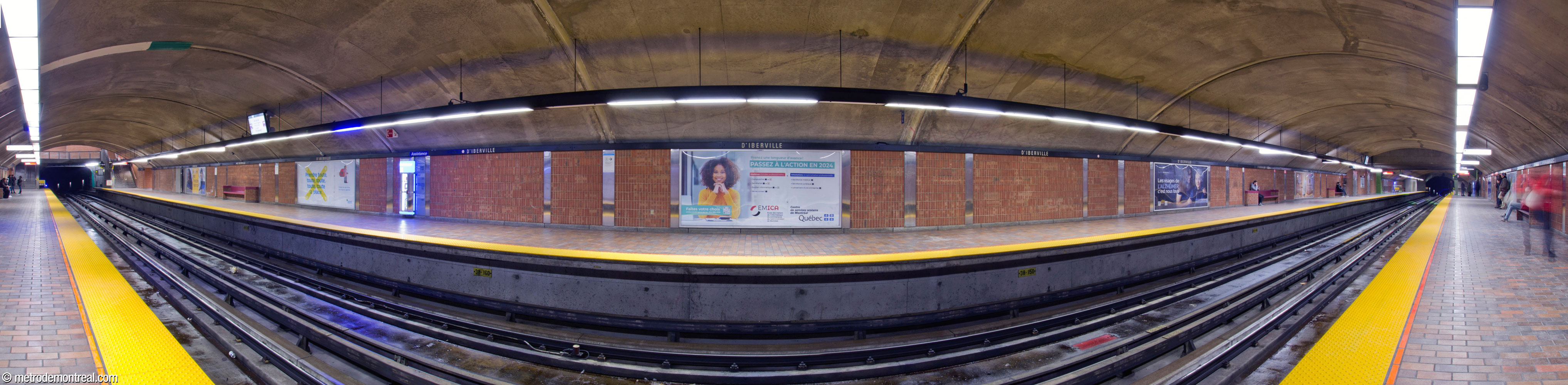 Panorama of the trainroom at D'Iberville metro station, seen from the Snowdon platform. The trainroom was built in tunnel. The walls are clad in plain bricks set vertically, divided by aluminum panels. The floor is tiled in terra cotta. At the east end (left), the parapet of the D'Iberville access is visible.