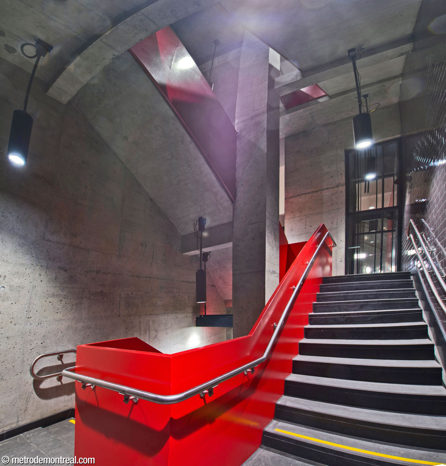 L’escalier auxiliaire accompagnant l’ascenseur principal est encadré par une balustrade écarlate vif et un mur d’accent noir. Cette section se trouve entre les niveaux du quai et du transept. Au fond s’élève la gaine d’ascenseur.