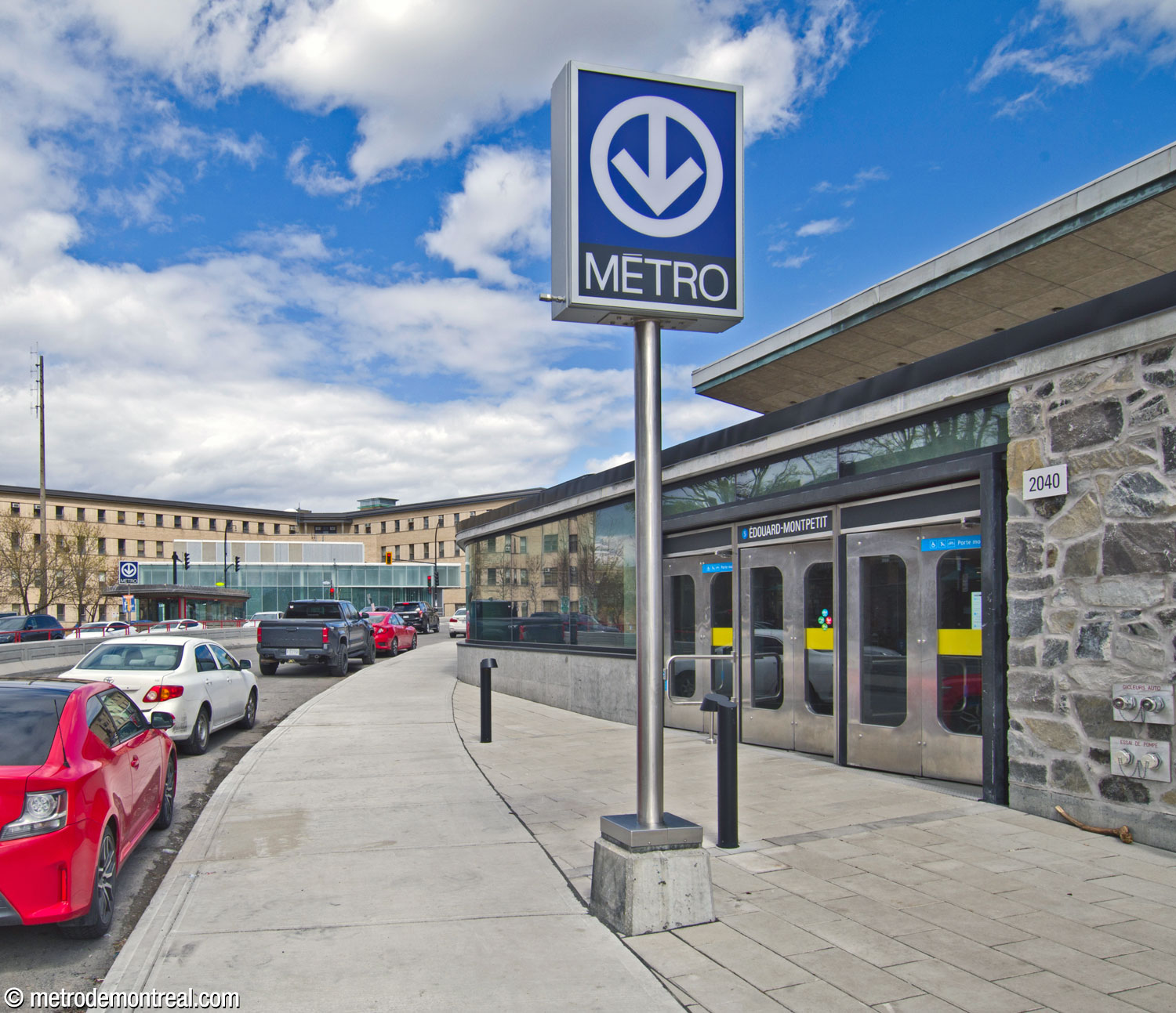 Vue le long du boulevard Édouard-Montpetit sur les trois accès de la station. En avant-plan à droite, l’accès Édouard-Montpetit/CEPSUM; au fond à gauche, l’édicule Vincent-D’Indy, et derrière lui l’édicule du REM.