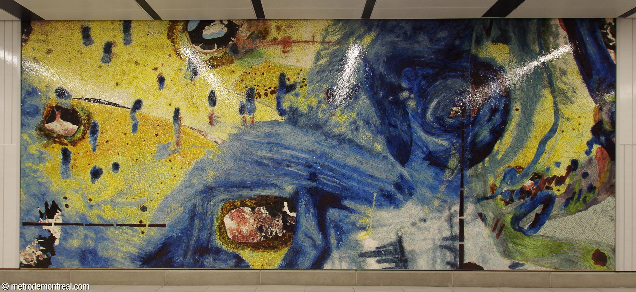 La troisième section de l’œuvre Le Mont habité de Manuel Mathieu, une mosaïque abstraite en jaune et bleu roi, située au bout du mur sud du corridor du transept, près de l’ascenseur vers le quai 2.