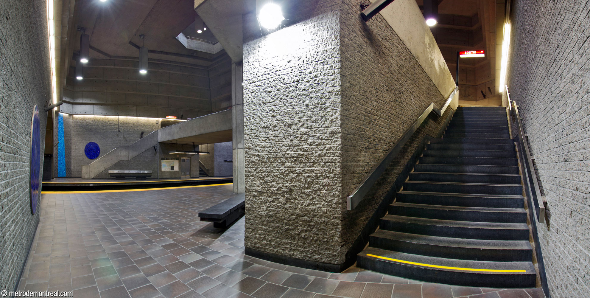 Le pied de l’escalier est vers le quai Côte-Vertu passe derrière la section élargie du quai. À travers les voies, à gauche, on aperçoit aussi l’escalier est vers le quai Montmorency, à découvert dans le grand volume.
