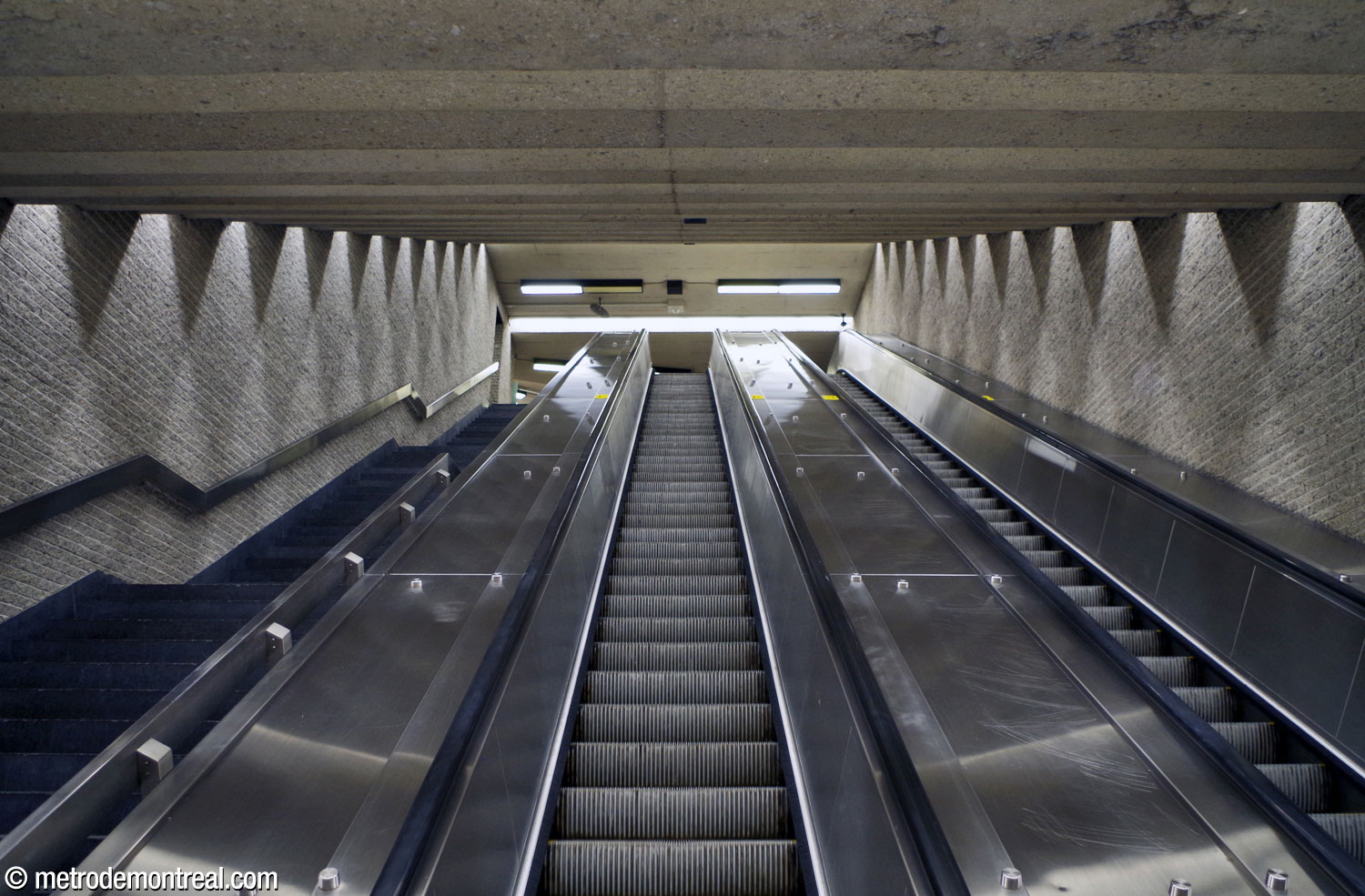 La cage d'escaliers entre les niveaux de la billetterie et de la passerelle. La disposition de l'éclairage au plafond crée un jeu d'ombres et de lumières sur les murs.