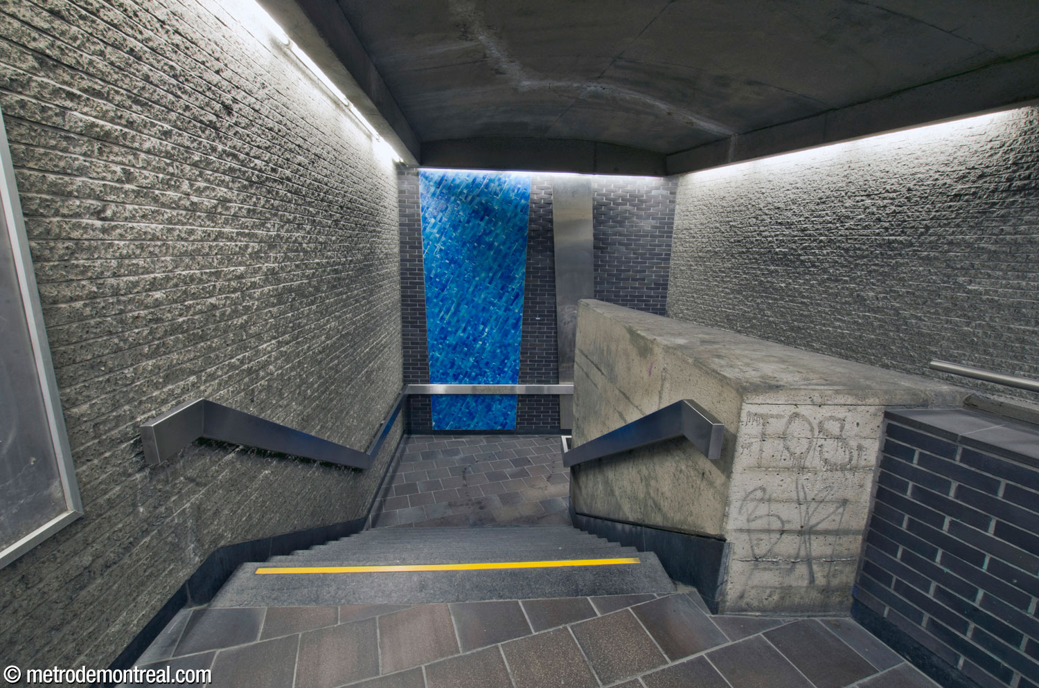 L’escalier ouest vers le quai Montmorency est accueilli par une excavation en niche. Ses formes obliques et irrégulières sont soulignées par un trapèze constitué de carreaux turquoise et par un panneau oblique en acier inoxydable.