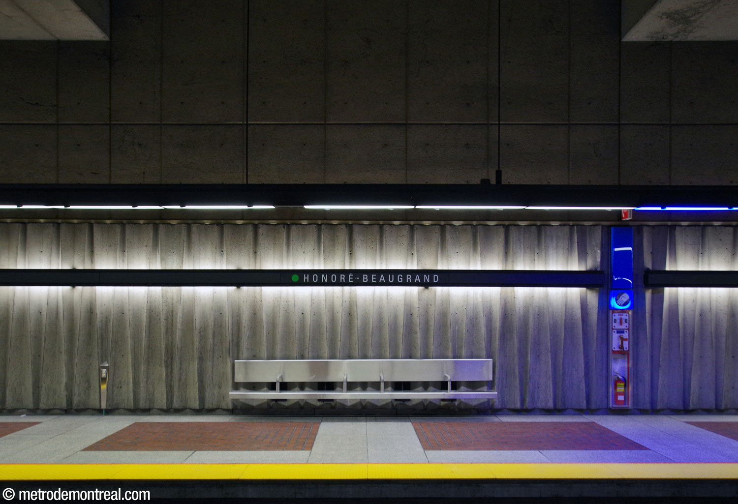La frise en béton sur le mur des quais, mise en valeur par l'éclairage théâtral dissimulé derrière les bandeaux de nom de la station.