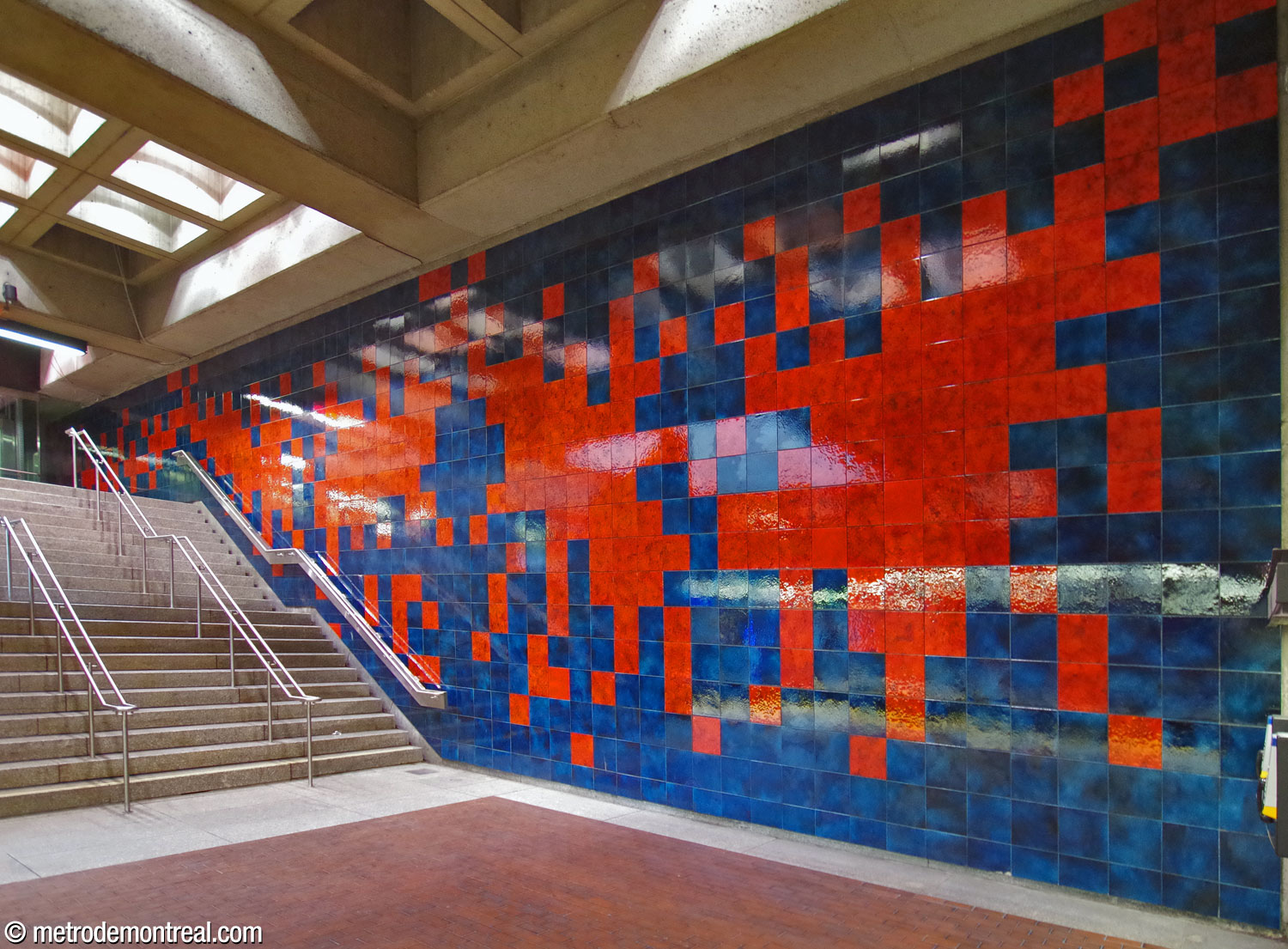 Murale en céramique de Jean-Paul Mousseau, avec des formes rouges sur un fond bleu, longeant l'escalier du quai d'arrivée.