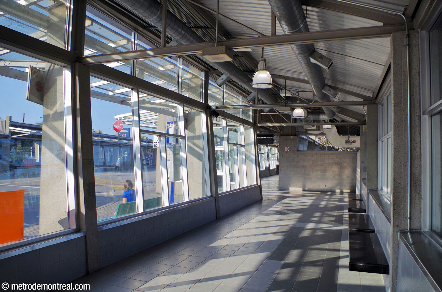 L'intérieur de la jetée sud du terminus d'autobus. Tant le mur avant qu'arrière du bâtiment en béton sont presque entièrement vitrés. Le plafond présente une charpente et des conduits à découvert.