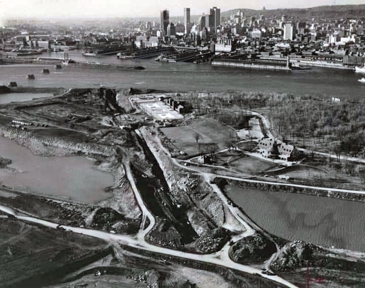 L'excavation à ciel ouvert de la station et des tunnels adjacents, en traversant les îles — elles-mêmes en construction — et le chenal entre elles.