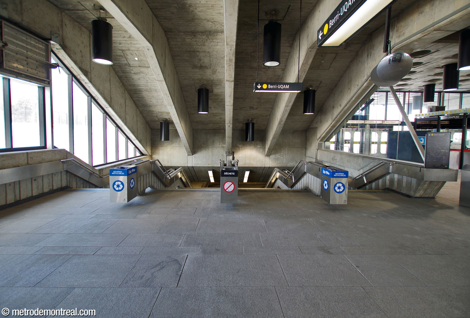 L'un des larges escaliers vers le quai Berri-UQAM, divisé en quatre voies par d'imposants murets en béton; ces derniers sont répétés par les poutres de la toiture.