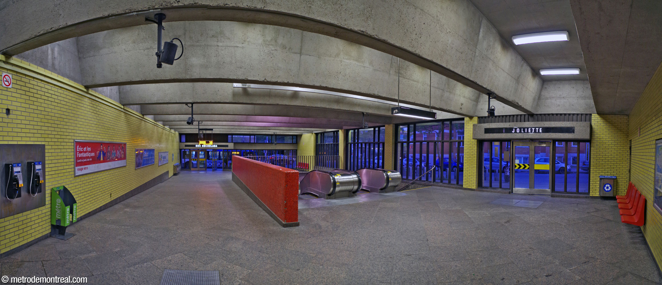 Intérieur de l'édicule Hochelaga Nord, vu depuis le fond. L’édicule s’ouvre sur les rues Hochelaga et Joliette. Le muret le long de la cage d’escalier est revêtu de mosaïque rouge, comme les accents dans les niveaux inférieurs. Des sièges identiques à ceux des quais sont également présents.