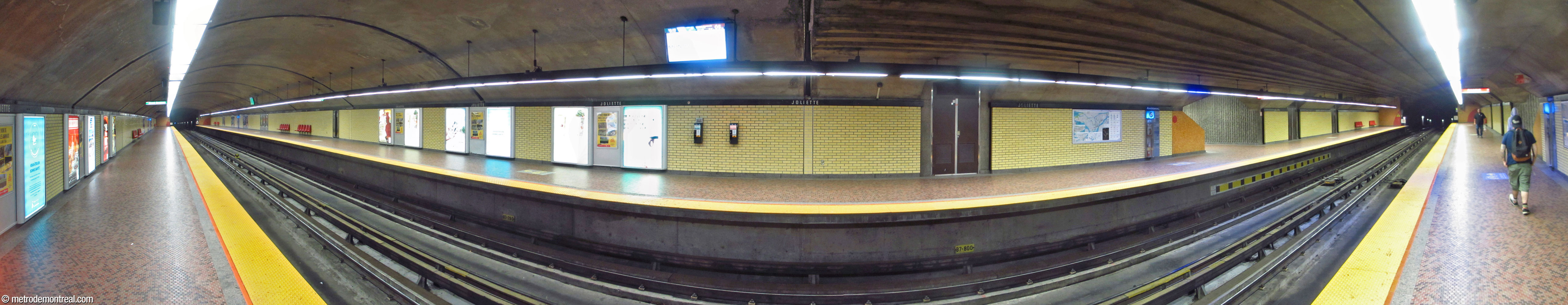 Panorama de la nef construite en tunnel, vue à partir du quai Honoré-Beaugrand. Les murs des quais sont revêtus sur leur pleine longueur de brique jaune mat, à l’exception des accents de mosaïque or et rouge-orange sur les tympans et les escaliers vers la salle de contrôle (centre-droite).