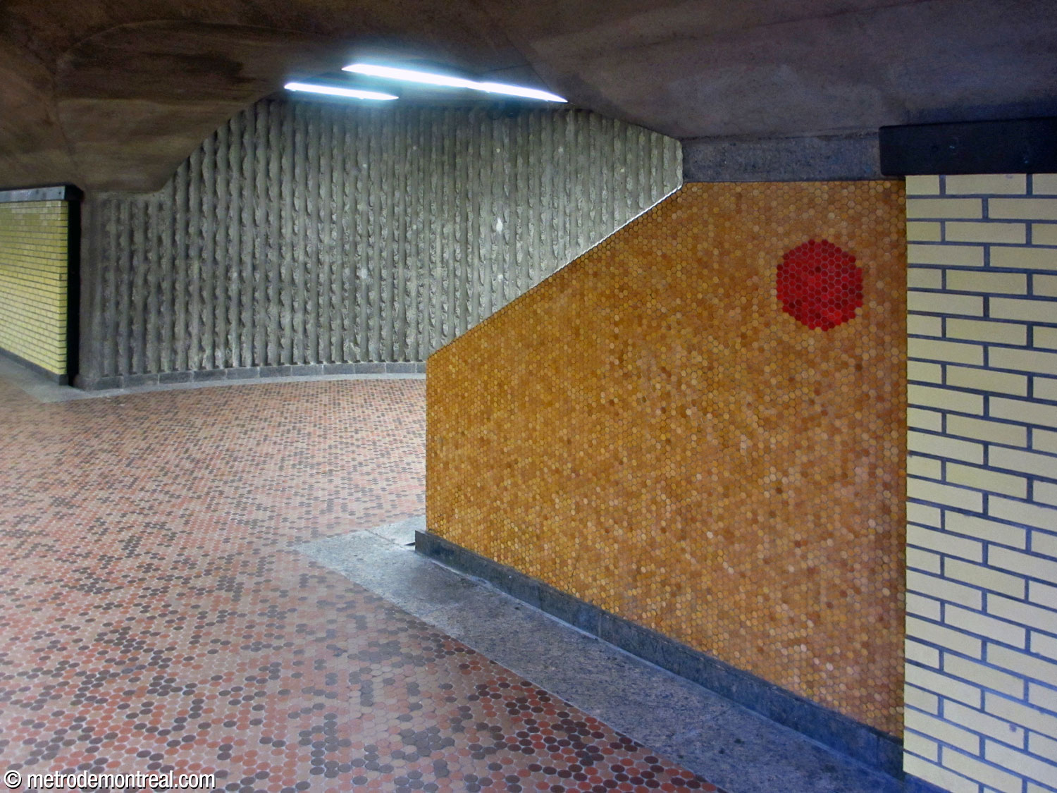 Entrée de la cage d'escalier reliant le quai Honoré-Beaugrand à la salle de contrôle. La section du mur le long de l'escalier est parée d'un carrelage mosaïque de couleur or ponctué par un petit cercle rouge.